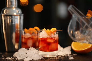Glasses of tasty Negroni cocktail and ice cubes on table against blurred background