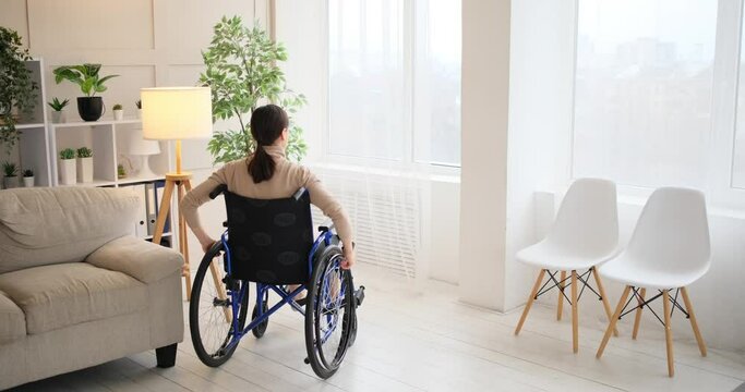 Woman in wheelchair looking out through window at home