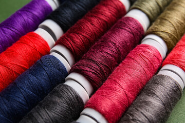 Different sewing threads on green background, closeup