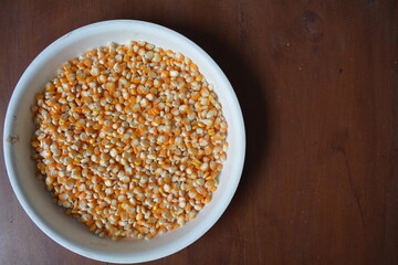 Orange corn kernels on a white tray, on a brown wooden texture background