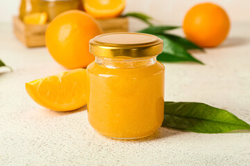 Glass jar of tasty orange jam on light background, closeup