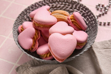 Bowl with tasty heart-shaped macaroons on pink background, closeup