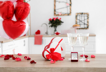 Glasses of champagne, gift boxes and engagement ring on table in kitchen
