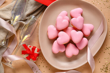 Plate with tasty heart shaped macaroons, gift box and glasses on beige background