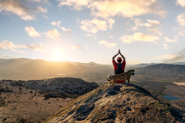 unknown person doing yoga outdoors on the top of the mountain with the company of a dog