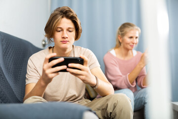 Portrait of interested excited teen boy playing online game on cell phone at home in free time. Teenagers internet gaming addiction concept ​