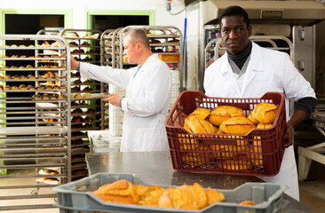 Professional bakers working in bakehouse, arranging fresh bakery goods ..
