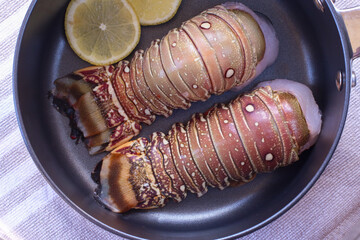 Fresh uncooked lobster tails in a pan with garlic butter glaze.
