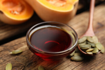 Glass bowl of pumpkin oil and seeds on wooden table, closeup