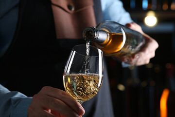 Bartender pouring white wine from bottle into glass indoors, closeup