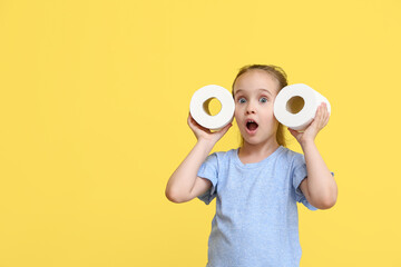 Shocked little girl with rolls of toilet paper on yellow background