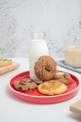 Varias galletas de chocolate con vaso de leche sobre plato rojo