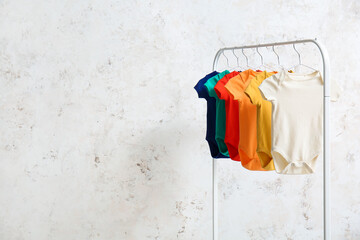Rack with colorful baby bodysuits near light wall