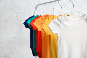 Rack with colorful baby bodysuits near light wall, closeup