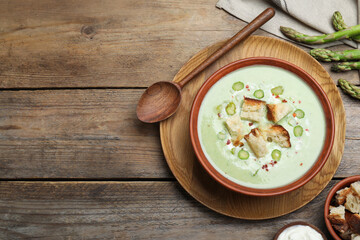 Delicious asparagus soup with croutons served on wooden table, flat lay. Space for text