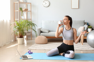 Fototapeta na wymiar Young woman in sportswear drinking water after training at home