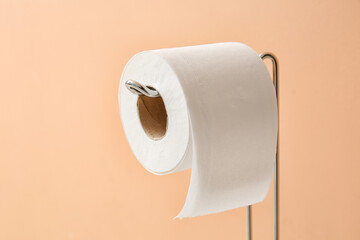 Holder with roll of soft toilet paper on beige background