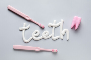 Toothbrushes, dental floss and word TEETH written with toothpaste on grey background