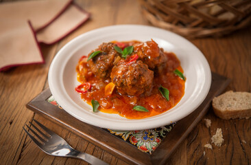 Almôndegas ao molho picante de tomate com folhas de manjericão e alho fatiado em fundo de mesa.