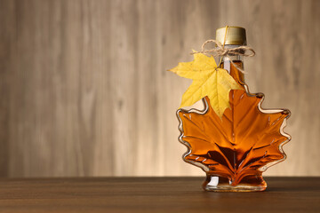 Leaf shaped bottle of tasty maple syrup on wooden table. Space for text