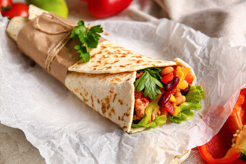 Parchment with delicious burrito on table, closeup