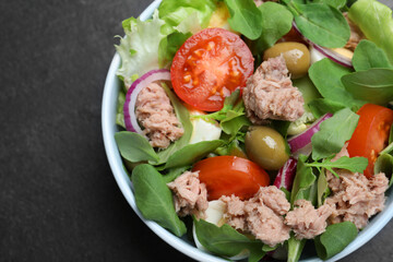 Bowl of delicious salad with canned tuna and vegetables on black table, top view