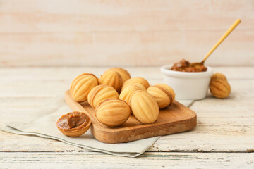 Board of tasty walnut shaped cookies with boiled condensed milk on light wooden background