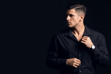 Fashionable gentleman adjusting shirt on dark background