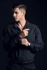 Fototapeta na wymiar Fashionable gentleman adjusting sleeve and looking aside on dark background