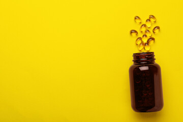 Overturned bottle with dietary supplement capsules on yellow background, flat lay. Space for text