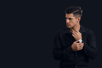 Fashionable gentleman with stylish wristwatch looking aside on dark background