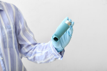 Woman holding asthma inhaler on light background