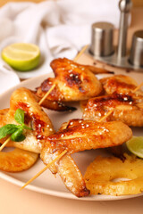Plate with grilled chicken wings skewers on beige background, closeup
