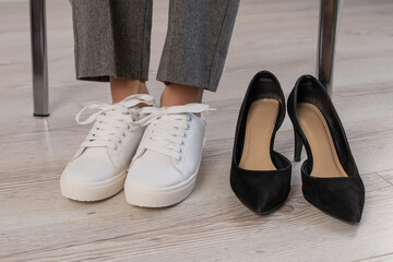 Close-up business woman takes off her shoes puts on white leather sneakers.