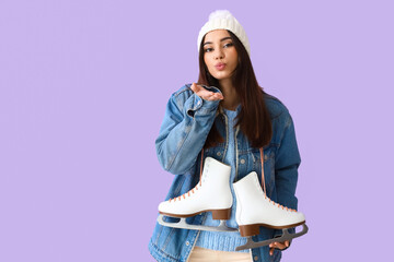 Beautiful young woman in winter clothes and with ice skates sending air kiss on color background © Pixel-Shot