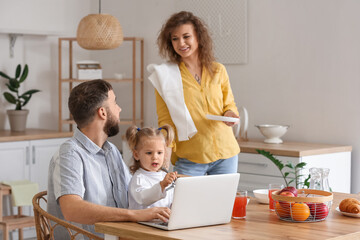 Happy young family with laptop in kitchen at home