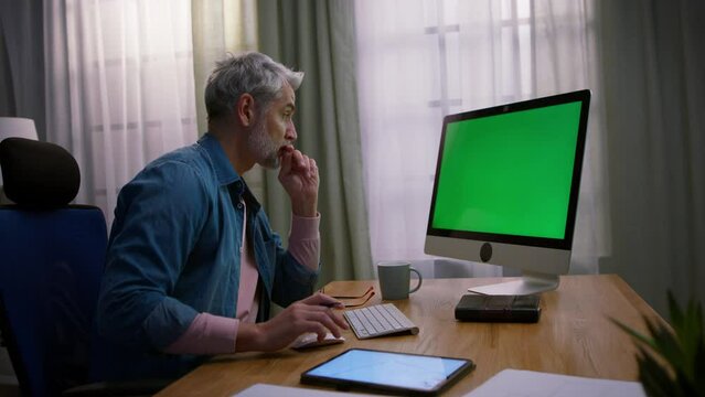 Mature man architect working on computer at desk indoors in office.