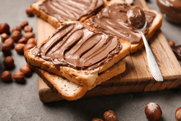 Wooden board of bread with chocolate paste and hazelnuts on table, closeup