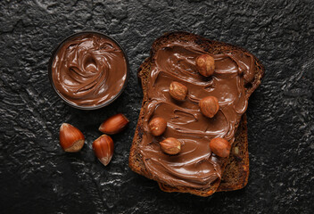 Bread with chocolate paste and hazelnuts on black background