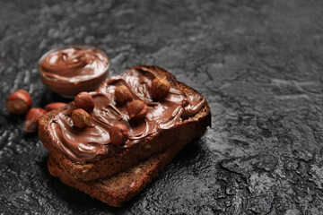 Bread with chocolate paste and hazelnuts on black background