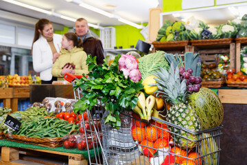 Shopping cart filled with fresh fruits and vegetables on background with family in store