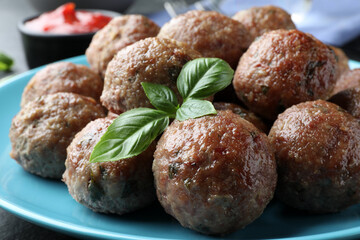 Tasty cooked meatballs and basil on plate, closeup view
