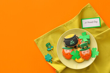 Plate with tasty gingerbread cookies for St. Patrick's Day celebration on orange background