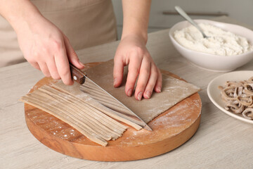 Woman making soba (buckwheat noodles) at wooden table, closeup