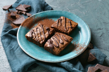 Plate with pieces of tasty chocolate brownie on blue background