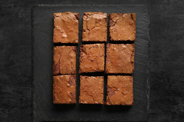 Board with pieces of tasty chocolate brownie on black background