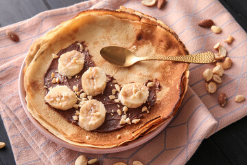 Plate of tasty thin pancakes with chocolate paste, cut banana and nuts on table