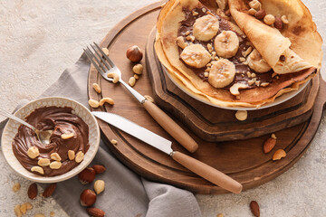 Plate of tasty thin pancakes with chocolate paste, cut banana and nuts on light background