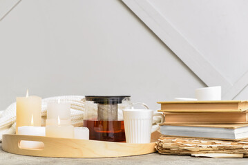 Tray with teapot, cup, candles and books on table near light wall