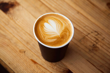 A warm cup of morning latte coffee with beautiful foam art standing on top of a rustic wooden table